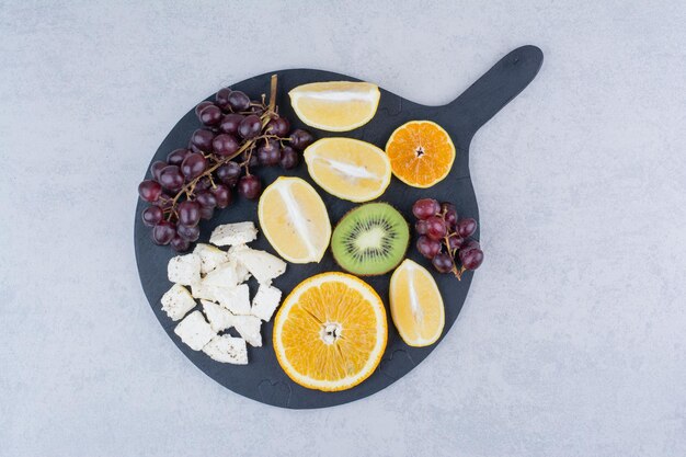 Темная разделочная доска свежих сладких фруктов и нарезанного белого сыра. Фото высокого качества