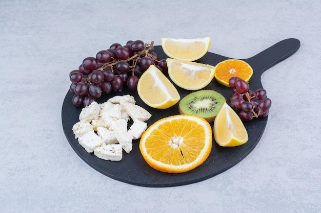 A dark cutting board of fresh sweet fruits and sliced white cheese.