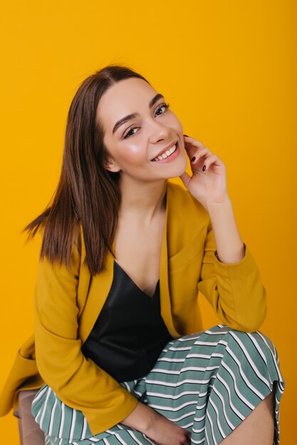 Dark-eyed cheerful woman in fashionable attire posing. Laughing gorgeous caucasian girl sitting.