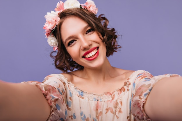 Donna carina dagli occhi scuri in corona che fa selfie con il sorriso. allegra ragazza bianca con i capelli ricci corti in posa.