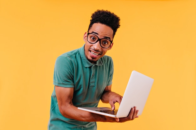 Dark-eyed international student posing with white laptop. Indoor photo of male freelancer typing on keyboard.