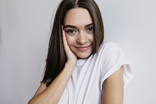 Dark-eyed young woman in white t-shirt looking with interest. Portrait of lovely female model standing.