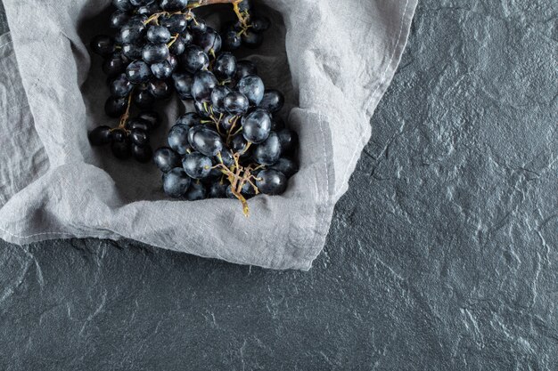 Dark fresh grape in basket on gray tablecloth.