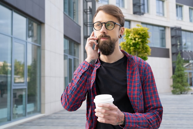 Dark-haired bearded man in eyeglasses talking via smartphone