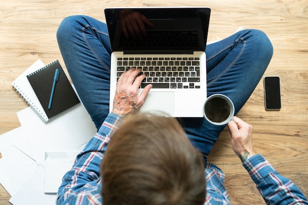 Dark-haired freelancer typing on laptop and drinking coffee