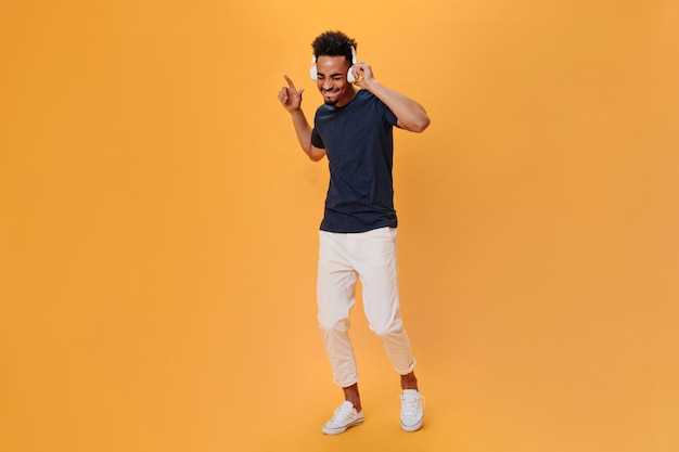 Dark-haired guy in T-shirt and white pants is dancing and listening to music