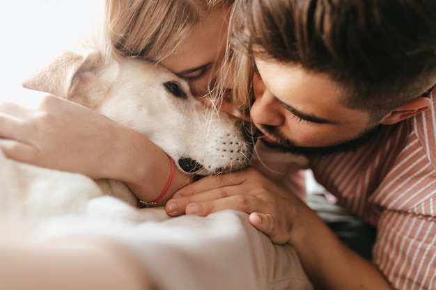 Dark-haired man and blond woman lovingly hug their Labrador. Portrait close-up of couple playing with dog.