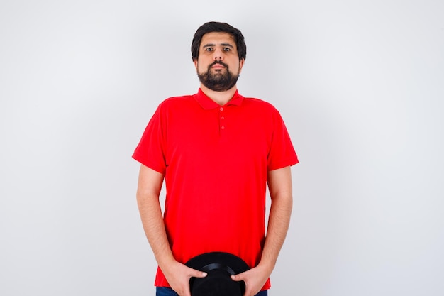 Free photo dark-haired man holding hat while looking away in red t-shirt front view.