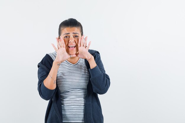 Dark-haired woman calling someone with loud voice in shirt