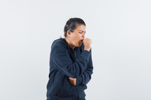 Dark-haired woman coughing in jacket and looking sick 
