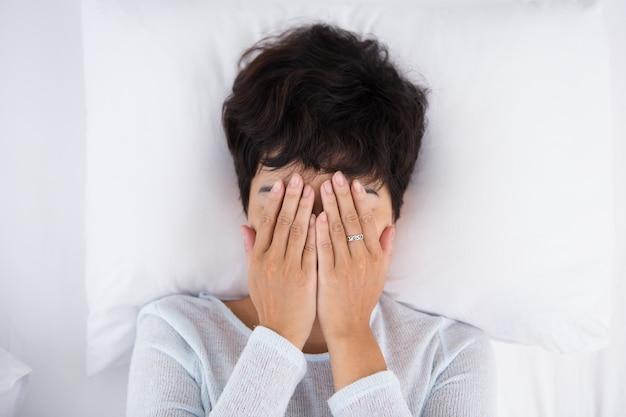 Free photo dark-haired woman covering face and lying in bed
