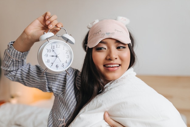 Dark-haired woman in excellent mood looks at alarm clock