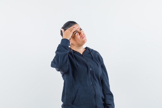 Dark-haired woman holding hand on forehead while thinking in jacket and looking pensive. front view.