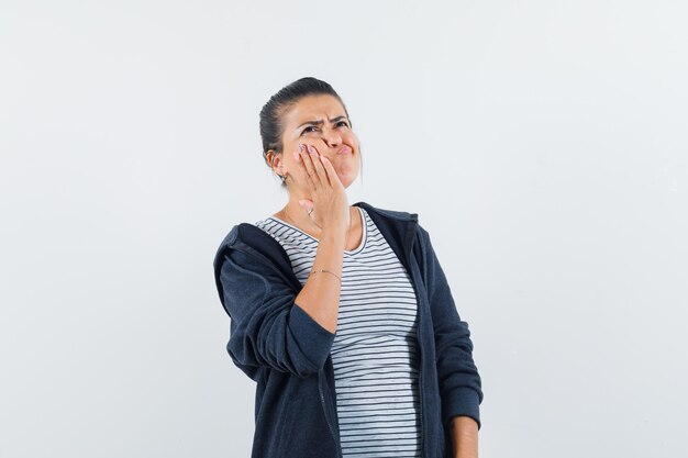 Dark-haired woman holding hand on her cheek in shirt