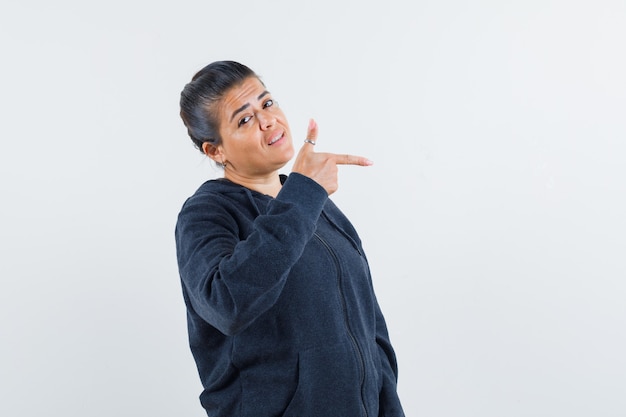 Dark-haired woman in jacket pointing aside 