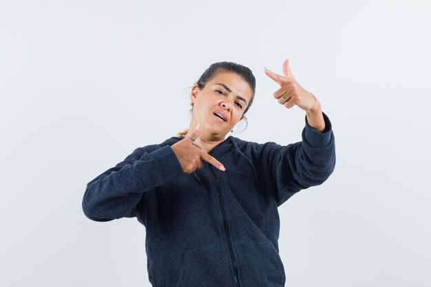 Dark-haired woman in jacket pointing up and down at the same time and looking hesitant 