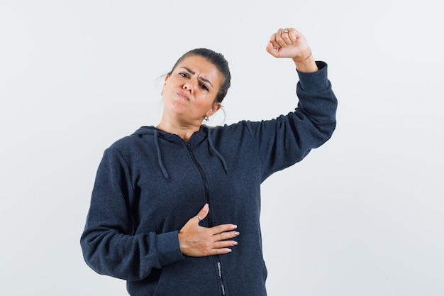 Dark-haired woman in jacket raising her arm and looking confident 