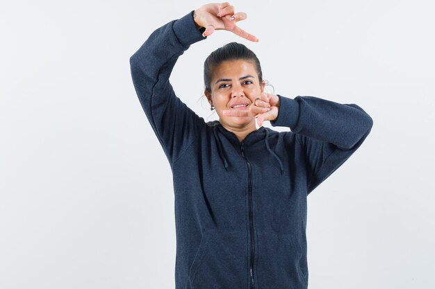 Dark-haired woman in jacket showing frame gesture 