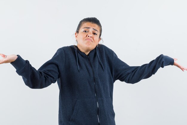 Dark-haired woman in jacket showing helpless gesture and looking displeased 