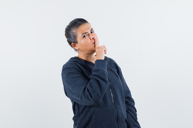 Dark-haired woman in jacket showing silence gesture and looking calm 