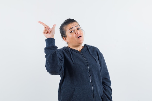 Dark-haired woman pointing aside in jacket and looking anxious 