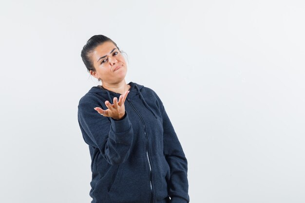 Dark-haired woman raising hand in jacket and looking discontented 