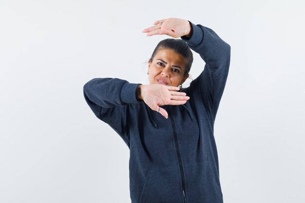 Dark-haired woman raising hands around head in jacket 