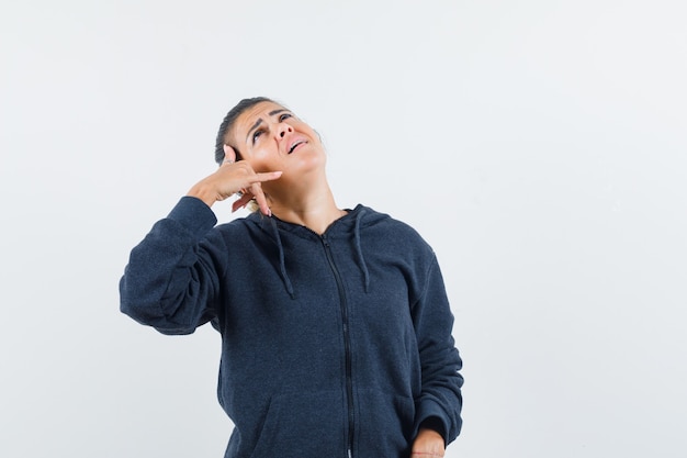 Dark-haired woman showing phone call gesture in jacket and looking talkative 