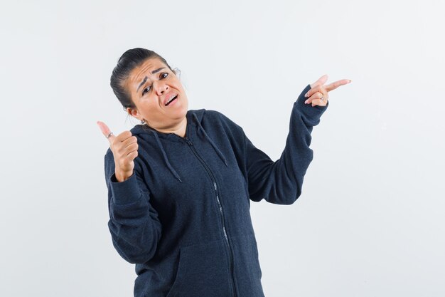 Dark-haired woman showing thumb up while pointing aside in jacket front view.