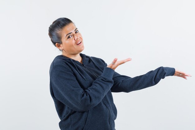 Dark-haired woman spreading her open palms at left side in jacket and looking expressive 