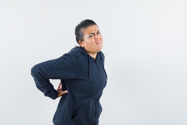 Dark-haired woman suffering from neck pain in jacket and looking uncomfortable . front view.