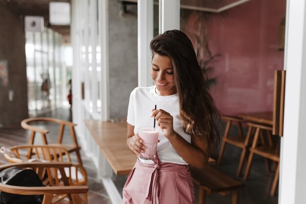 Dark-haired woman with smile stirring strawberry yogurt