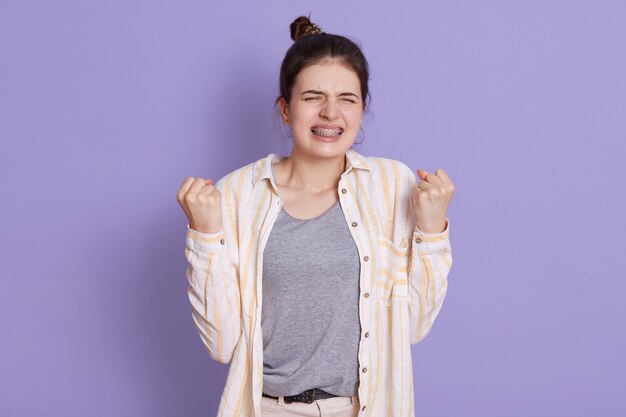 Dark haired young woman in braces clenching fists with angry facial expression