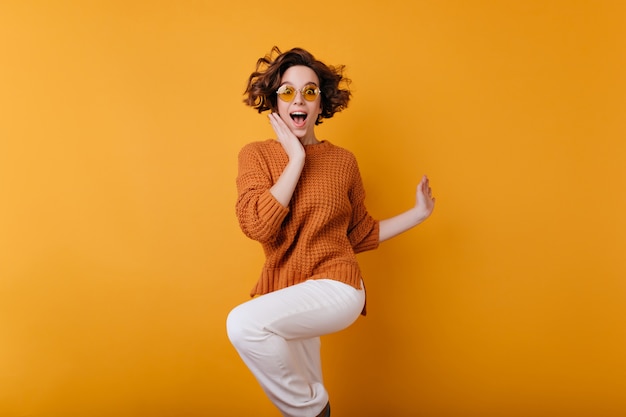 Dark-haired young woman jumping and expressing happiness.  portrait of surprised positive girl with short haircut and arm tattoo dancing with smile.