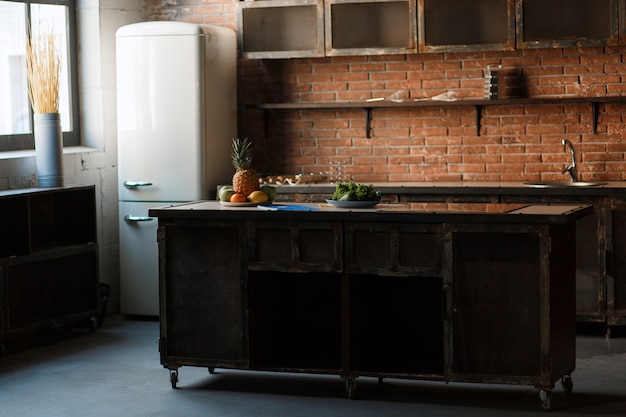 Темная чердак кухня с красной кирпичной стеной. Кухонный стол Столовые приборы, ложки, вилки, фрукты для завтрака