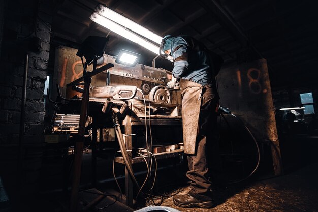 На темном металлургическом заводе занятой человек работает на своем рабочем месте.