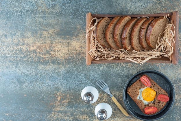 A dark pan with fried egg and slices of brown bread on marble background