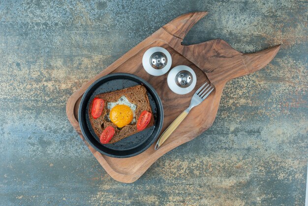 A dark pan with fried egg and slices of brown bread on wooden board