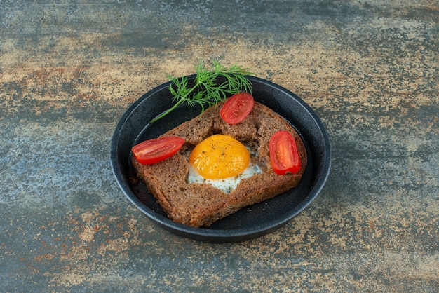 A dark pan with fried egg and tomato on marble background