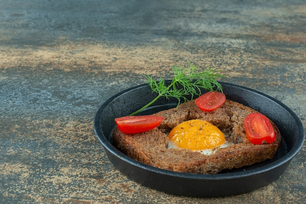 Free photo a dark pan with fried egg and tomato on marble background