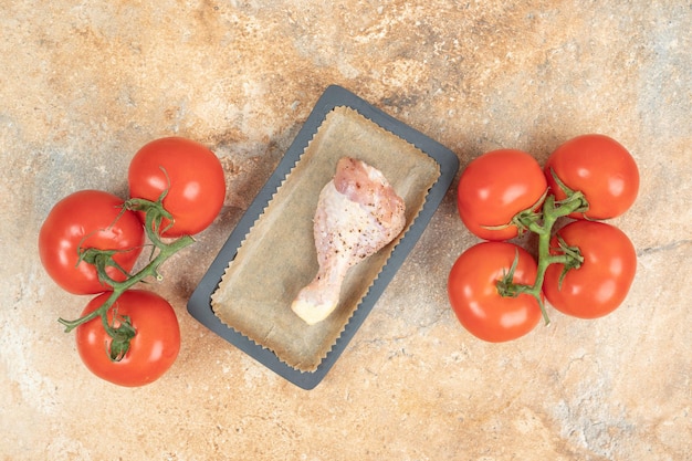 A dark pan with tomatoes and chicken legs on marble surface.High quality photo