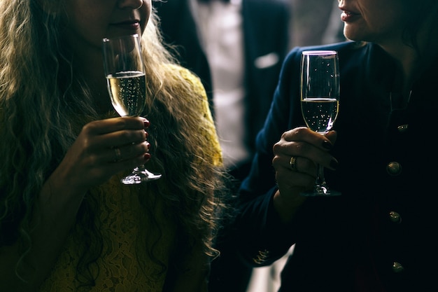 Dark picture of talking women and champagne flutes in their arms