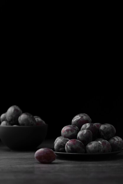 Dark plate and bowl with plums on a dark background