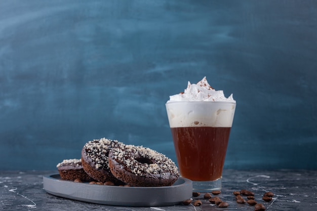 Dark plate of chocolate donuts with coconut sprinkles and delicious coffee on marble background. 