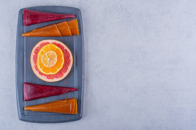 Dark plate of delicious dry fruit pulps and grapefruit on stone.