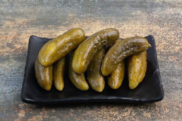 A dark plate full of delicious pickled cucumbers on white background . High quality photo