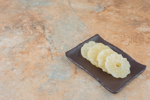 A dark plate full of dried healthy pineapple