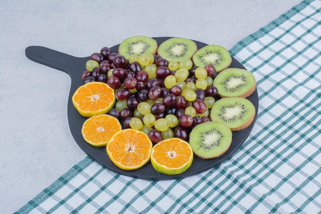 A dark plate full of grapes, kiwi and orange on tablecloth. High quality photo