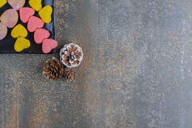 솔방울과 함께 심장 모양의 설탕 젤리 사탕으로 가득 찬 어두운 접시. 고품질 사진
