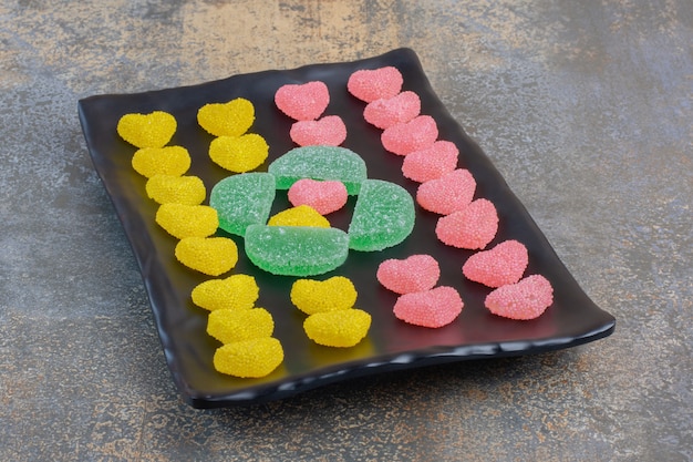 A dark plate full of heart shaped sugary jelly candies with pinecones. High quality photo